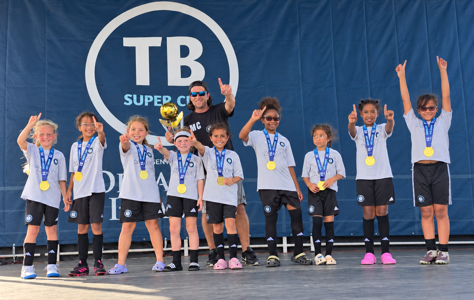 The U9 LASE Lionesses celebrating their Tampa Bay Super Cup win with their coach, trophy and medals
